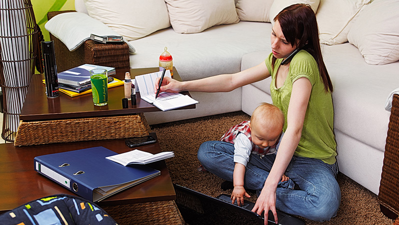 Junge Mutter mit Baby arbeitet zu Hause am Laptop und telefoniert